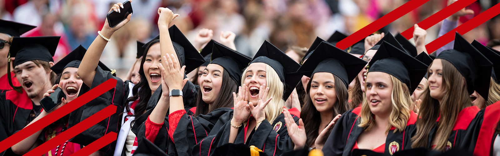 Group of graduates wearing academic attire smiling and cheering.