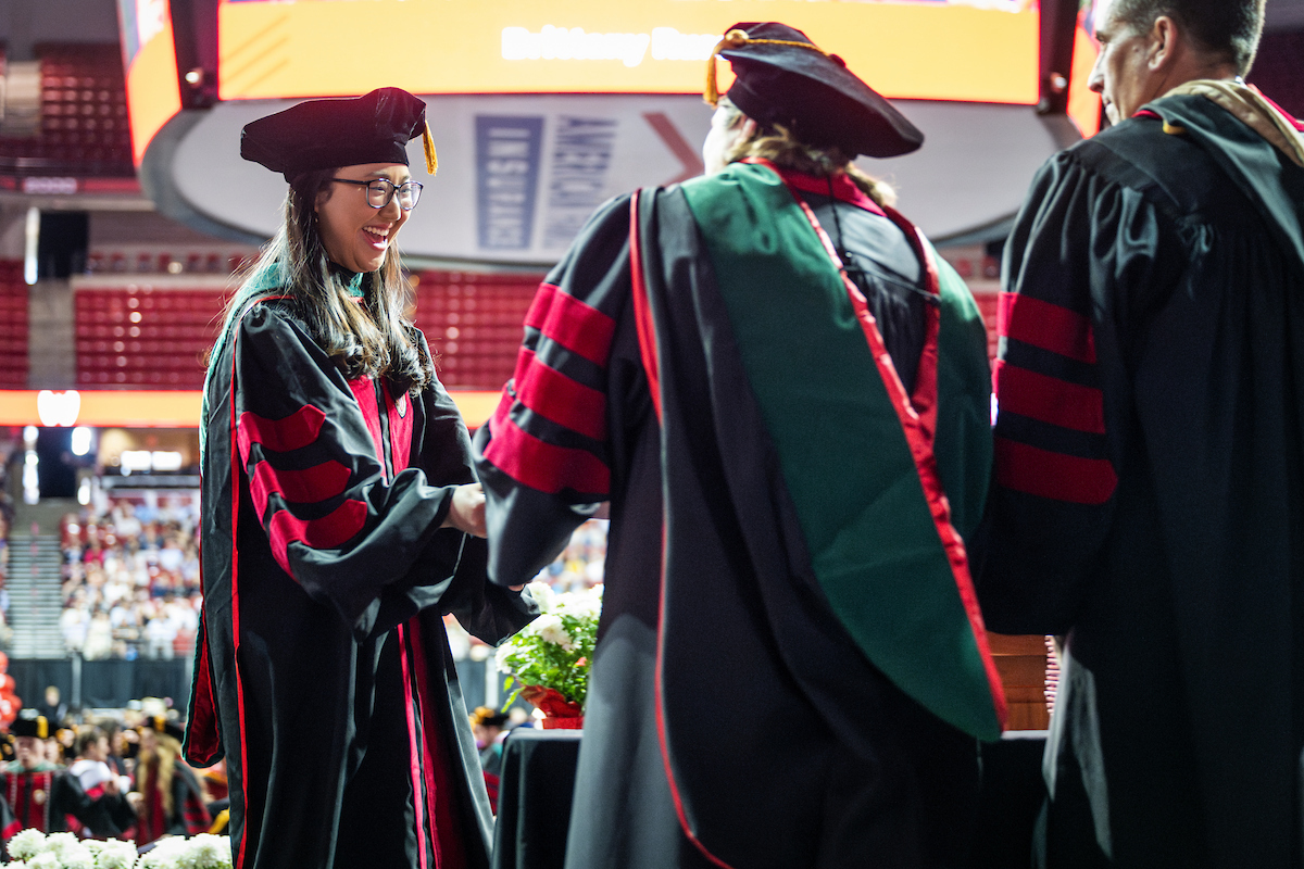 Graduate in academic attire smiles as they cross the stage receiving diploma.