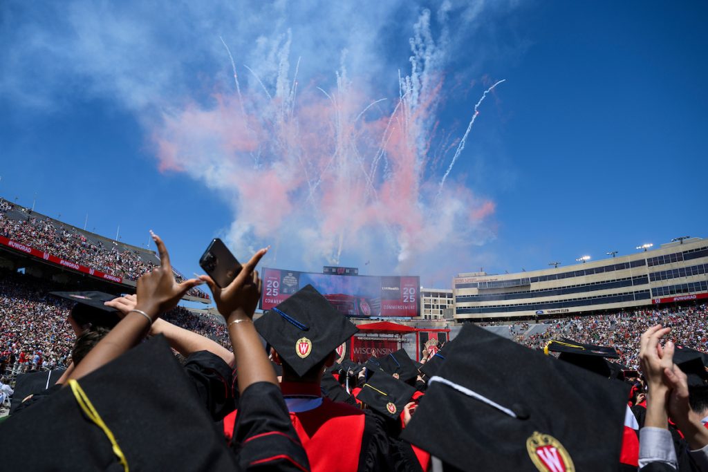 Graduates admire the fireworks display at the conclusion of UW–Madison's spring commencement ceremony and flash the W sign