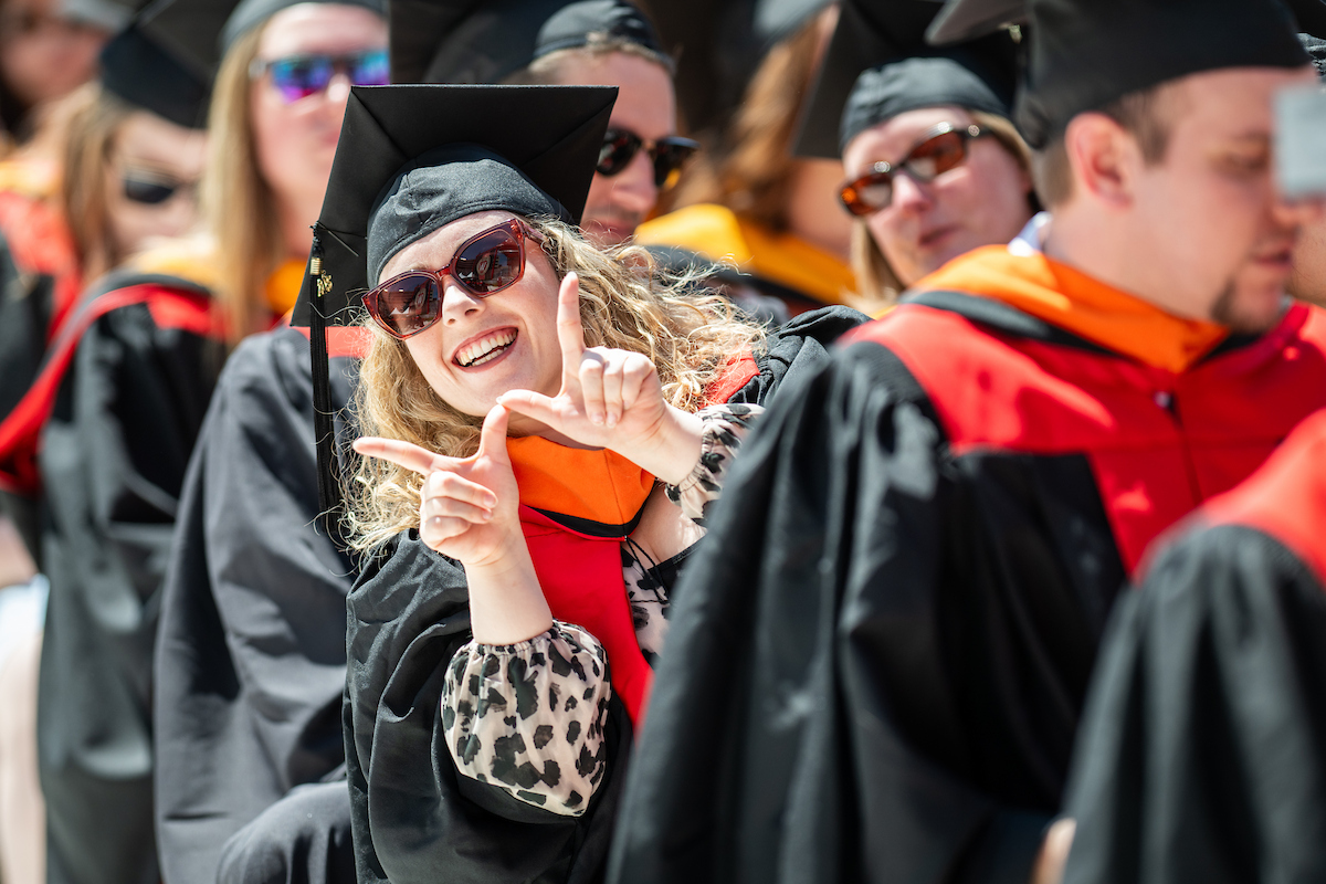 Graduate wearing sunglasses smiles wide and flashes the W sign